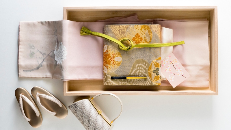 桐材の収納ケースに入っているピンクの着物と帯など
箱の横に添えられたバッグと草履