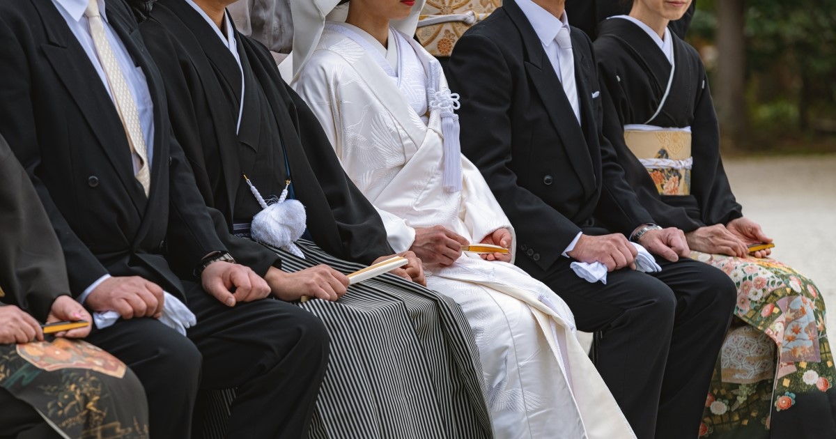 黒留袖、白無垢を着た女性と羽二重黒紋付を着た男性と洋装の男性が並んで座る様子