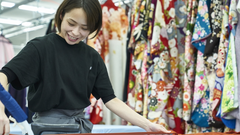 着物に囲まれてプレス（仕上げのアイロン掛け）作業をしているディアハートのクリーニングスタッフ